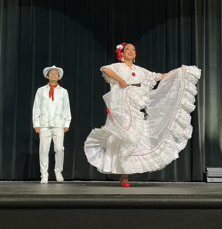 Teen folklorico dancers performing a traditional Mexican folk dance on stage